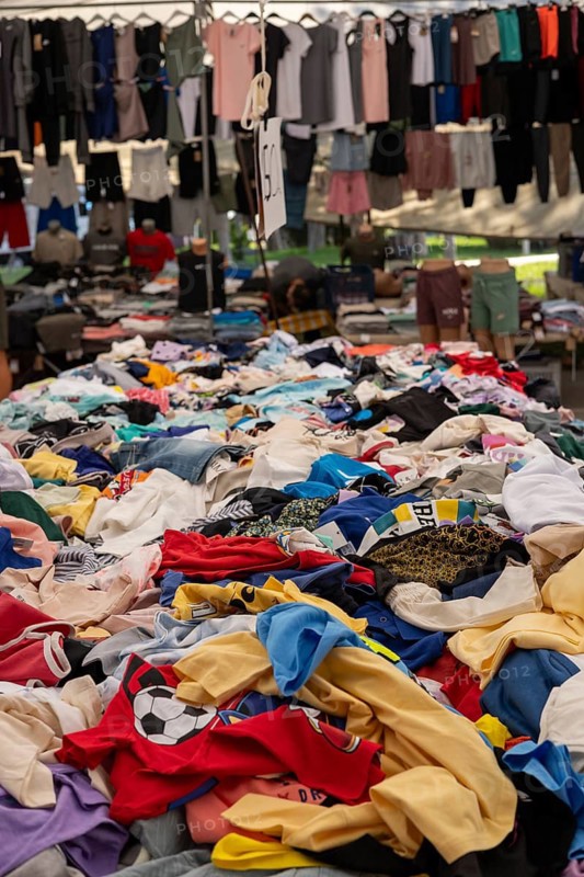 Piles of colorful clothes at a busy outdoor market stall