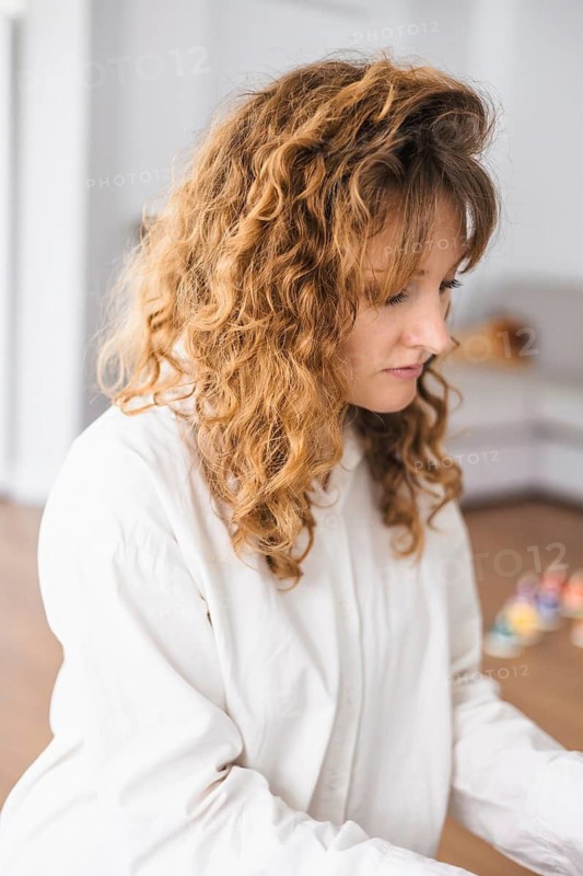 A woman with curly hair appears thoughtful in a cozy home setting