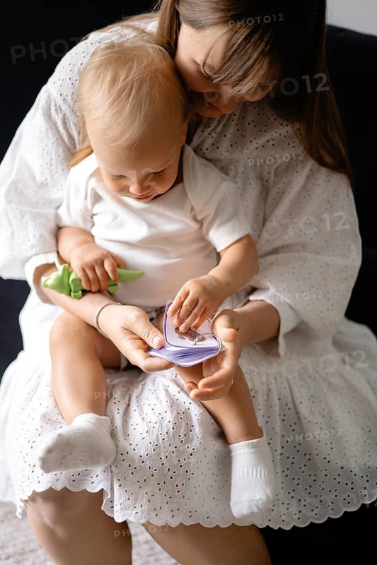 Woman in a white dress holding a baby with a toy, showcasing a nurturing bond