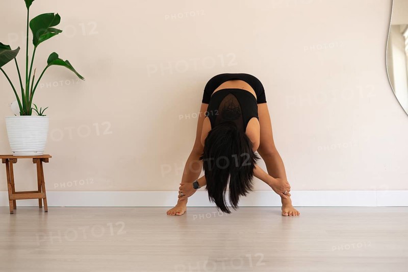 Woman practicing a yoga pose, bending forward in a serene studio environment