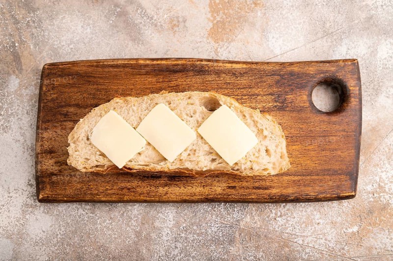 Slice of homemade bread with butter on cutting board on brown concrete background, close up, top view, flat lay