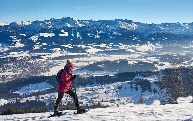 Nice and active senior woman snowshoeing in in the snow covered Allgaue alps above the valley of river Iller, Immenstadt, Bavaria, Germany