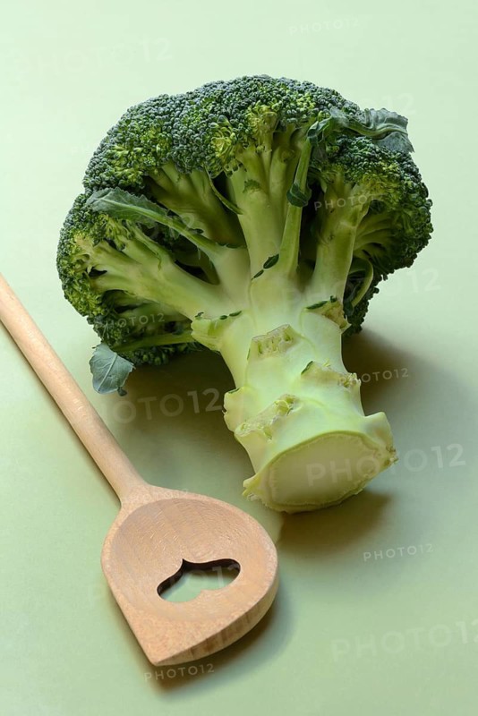 Broccoli with cooking spoon on green background