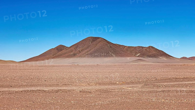 Lonely mountain in the middle of a vast, dry desert landscape under blue skies, The Moon Valley in the Atacama on the Altiplano in the Aden near San Pedro de Atacama in Chile