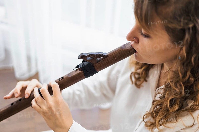 Close-up of a woman with curly hair playing a wooden flute in concentration