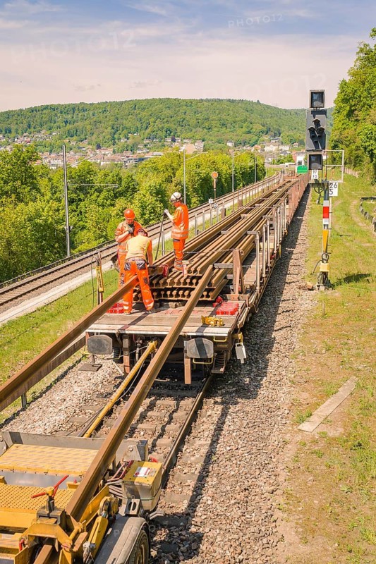 Workers in orange on rail cars working on the tracks next to signals, Leonhard Weiss construction site to renovate the train station and build the overhead line, Waldshut, Germany