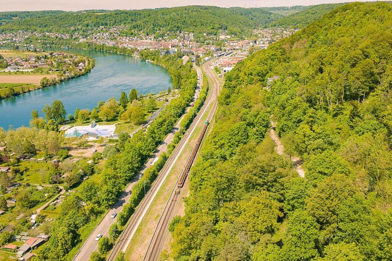 Railway line along a river in a wooded and urban environment in spring, construction site by Leonhard Weiss to renovate the station and build the overhead line, Waldshut, Germany