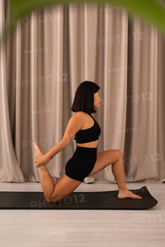 Woman holds yoga pose on mat, embracing tranquility, with plant and soft curtains nearby