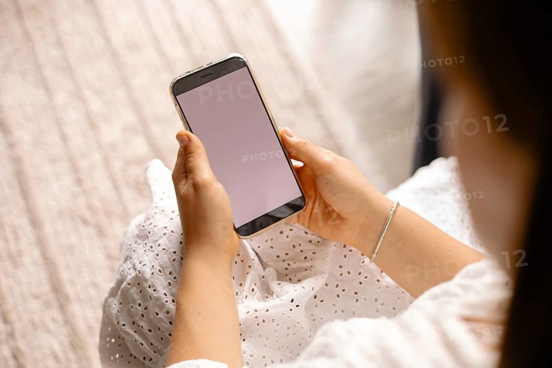 A blank smartphone screen is held in both hands, focused and casual atmosphere over a white dress