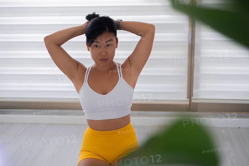 Woman in workout clothing stretching with her arms raised indoors