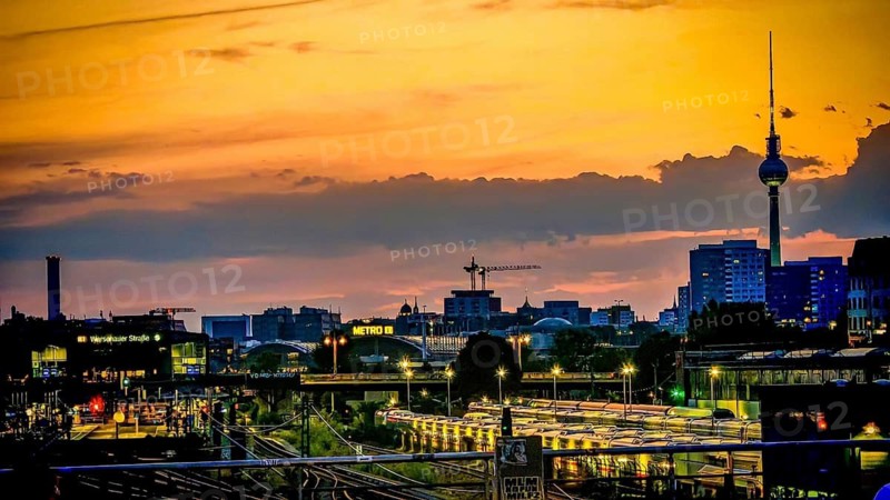 View of railway tracks from Modersohn Bridge, skyline at sunset with television tower and illuminated buildings in the foreground, Friedrichshain, Berlin