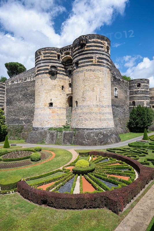 Monumental castle complex from the 13th century with distinctive tower architecture, nestled in a well-kept park and garden landscape with symmetrical patterns in the deep ditch in front of the fortress walls, Château d'Angers, Angers, Maine-et-Loire, Pays de la Loire, France