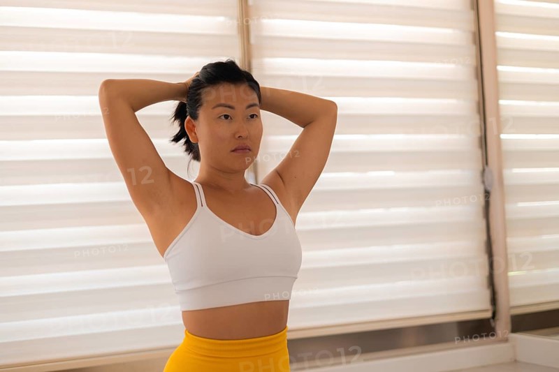 Woman standing with hands on head looking thoughtfully at blinds