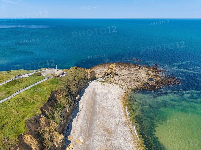 Aerial view of the historic Pointe du Hoc headland on the cliffs of Normandy. The green cliff rises prominently into the blue Atlantic. The numerous, deep bomb craters from the Second World War, which still shape the landscape today, are clearly visible. At this former base of the German Wehrmacht, a decisive battle took place on June 6, 1944 during the Allied Invasion, D-Day, Operation Overlord, Omaha Beach, Calvados Department, Normandy, English Channel, France