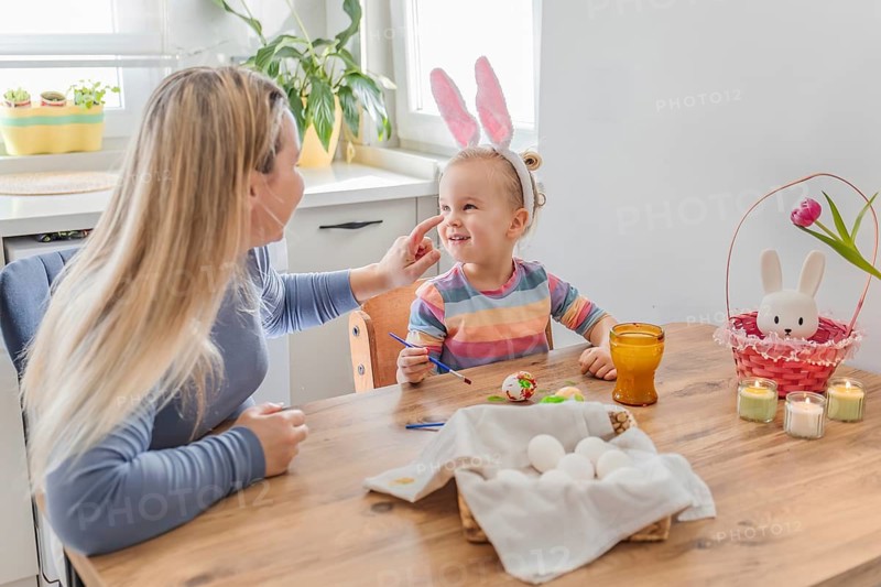 Mother and toddler girl daughter painting Easter eggs at home in modern kitchen. family tradition, spring celebration and holiday preparation
