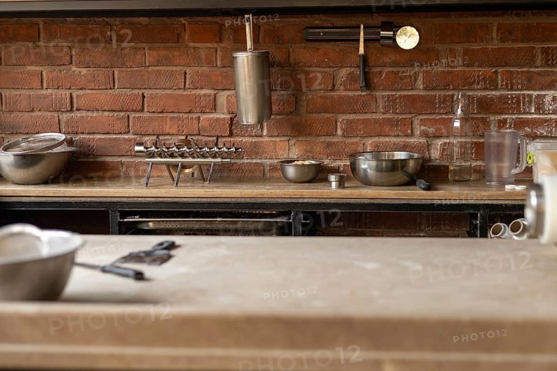 A neatly organized kitchen countertop featuring various metal cookware, including bowls and tools, set against a rustic brick wall, ideal for meal preparation. Modern restaurant or bakery or small noodle factory