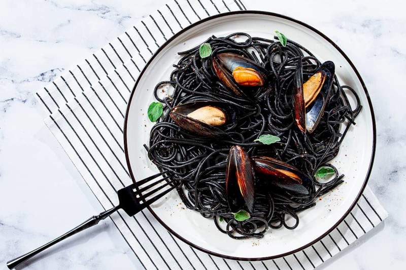Black spaghetti with mussels, on a white plate with a fork, on a striped napkin, marble background, homemade, no people