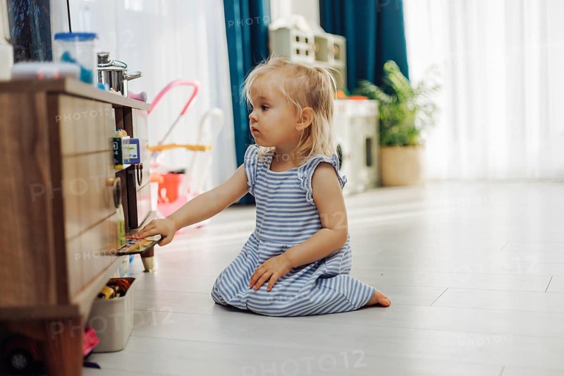 Child girl interacts with a storage unit filled with toys in a sunny indoor space