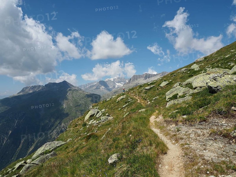 Mountain trail with view of majestic mountains under blue sky with clouds, Bellwald, Goms, Canton of Valais, Switzerland