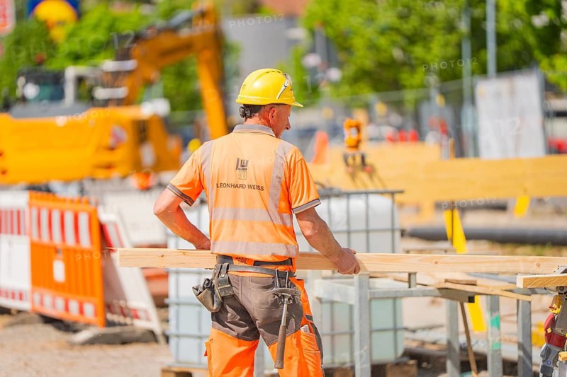 Construction worker with helmet and orange vest working on a construction site, in the background an excavator, Leonhard Weiss construction site to renovate the train station and build the overhead line, Waldshut, Germany