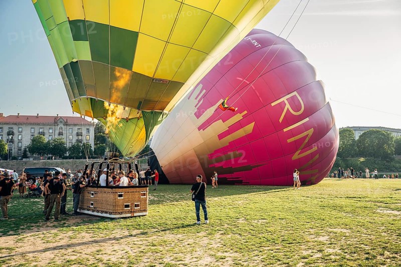 Vilnius, Lithuania, 08 05 2022: Hot air balloons in Vilnius. Multi-colored hot air balloons on the ground before takeoff. Lots of balloons in the field, Colorful hot air balloons being prepared for launch in a grassy area with people and buildings nearby, Vilnius, Lithuania