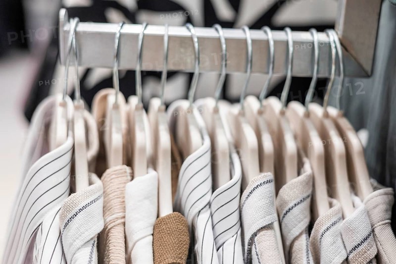 A rack displaying neatly arranged striped and solid shirts in a retail store. The shirts are hanging on wooden hangers, showcasing various colors and patterns