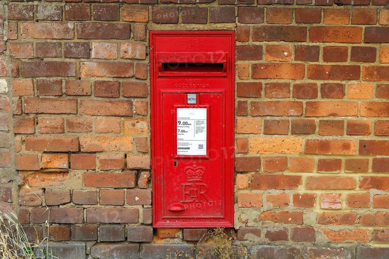 Red Royal Mail postbox bearing the ER cipher set into a weathered brick wall, Bierton, Buckinghamshire, United Kingdom