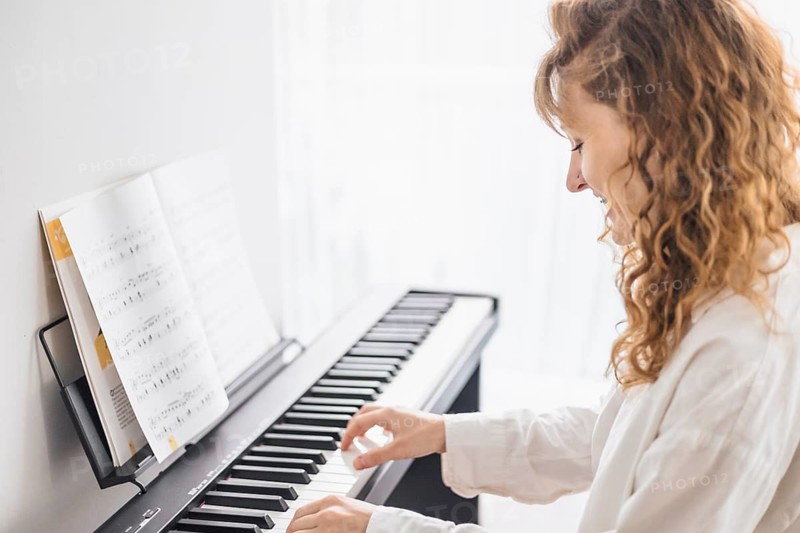 A woman plays a digital piano with focus, sheet music is in front of her