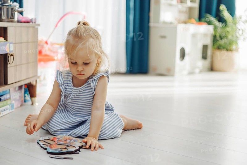 Young girl focused on a colorful toy while sitting quietly on the floor indoors. Wooden eco-friendly toys for developing skills in game