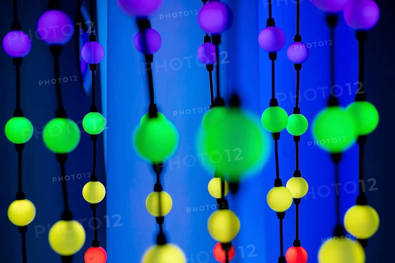 Colorful decorative beads in various sizes and colors, hanging against a vibrant background. The scene is bright and playful, ideal for festive themes