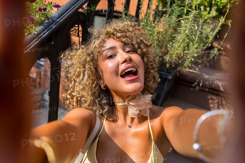 Joyful woman with curly hair captures a selfie on a brownstone stoop, enjoying urban summer life in manhattan, embodying youthful happiness and city lifestyle