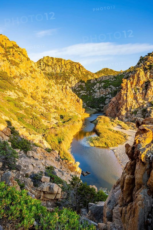 A small river flowing through the mountains into the sea, past a sandy beach in Costa Paradiso on a sunny evening, Sardinia, Italy