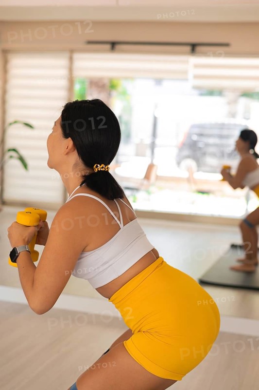 Woman holding dumbbells while squatting in a bright living room during a workout