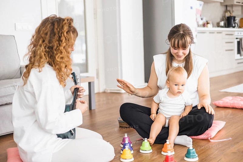 Two women and a baby interacting cheerfully in a room with musical elements