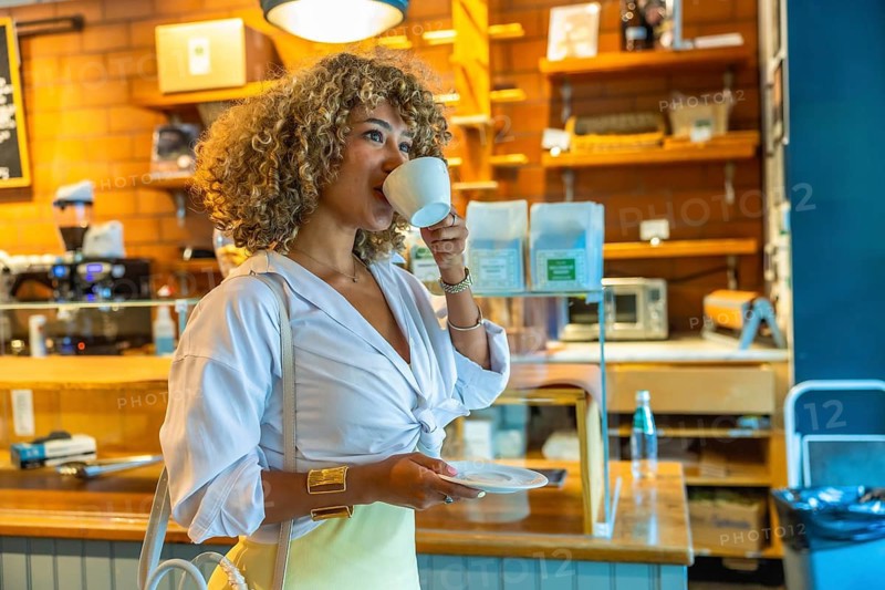 Woman standing in an urban coffee shop, drinking a hot beverage from a white mug, embodying the vibrant lifestyle of manhattan residents