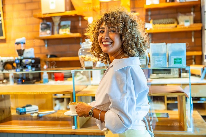 Smiling woman with curly blonde hair holding a cup of coffee inside an urban cafe, reflecting a casual manhattan lifestyle experience and modern city living