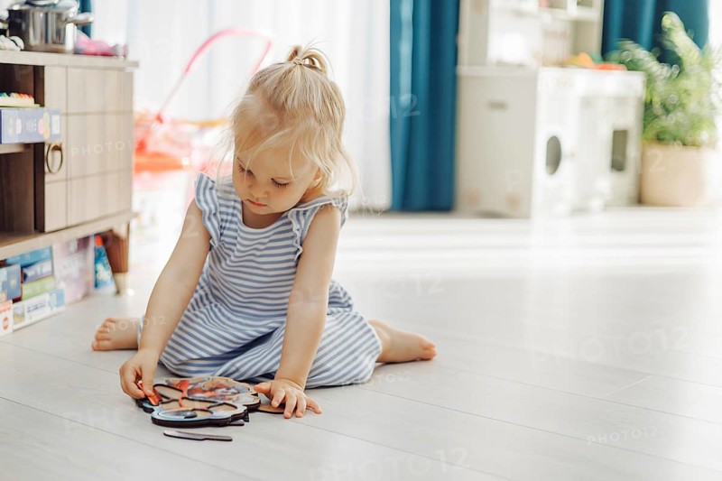 A young child sitting on a floor assembling a puzzle in a softly lit room