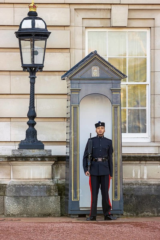 A Queen's Gurkha Signals guardsman stands sentry beside an ornate lamp post at Buckingham Palace, London, England, United Kingdom
