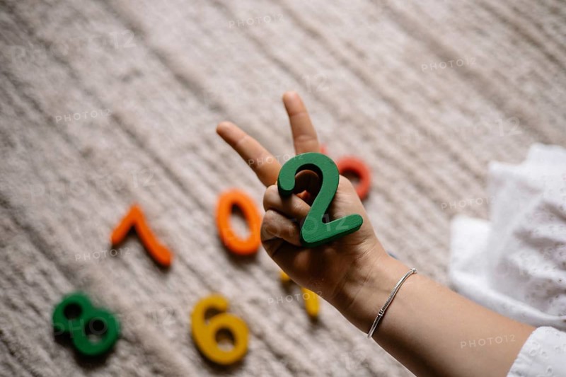 Hand showing a peace sign, holding the number two among scattered colorful numbers