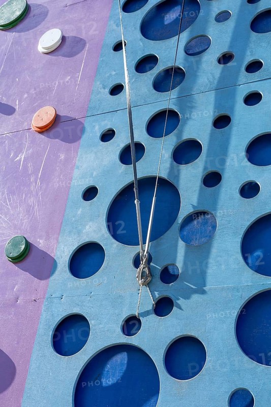 Tackling a colorful tall climbing wall tower. The setting offers a fun and engaging outdoor activity surrounded by vibrant architecture. Activities and sport training for children
