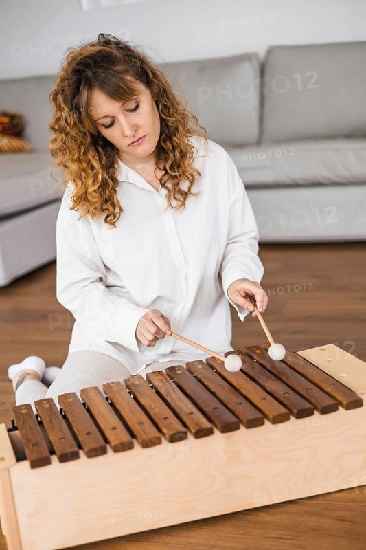 Woman in white playing marimba in a cozy room with a soft focus