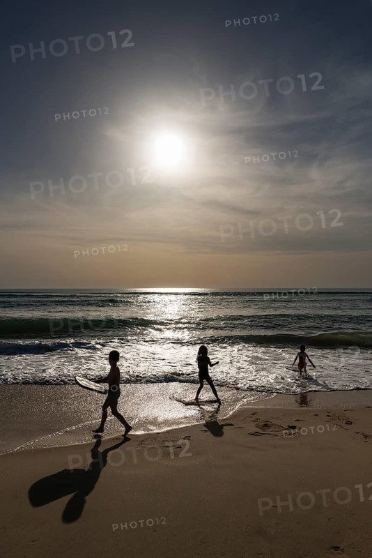 Silhouette of children playing against the evening sun on the Atlantic Ocean, France