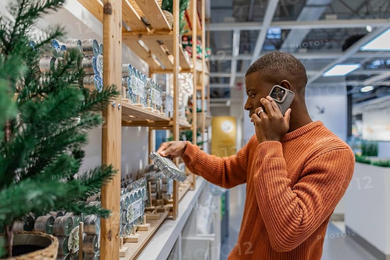 Man is standing in store looking at home decor items on shelves. He is holding a phone while reaching for a product