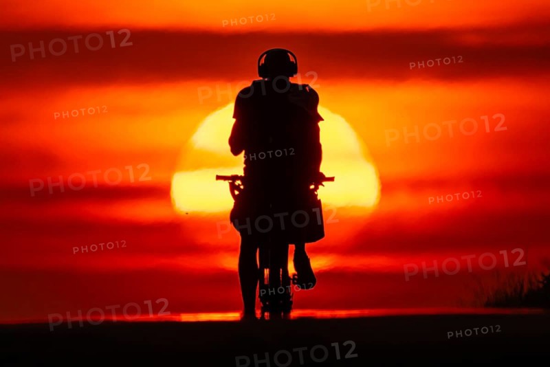 A cyclist rides towards the rising sun on a dirt road near Frankfurt am Main, Frankfurt am Main, Hesse, Germany