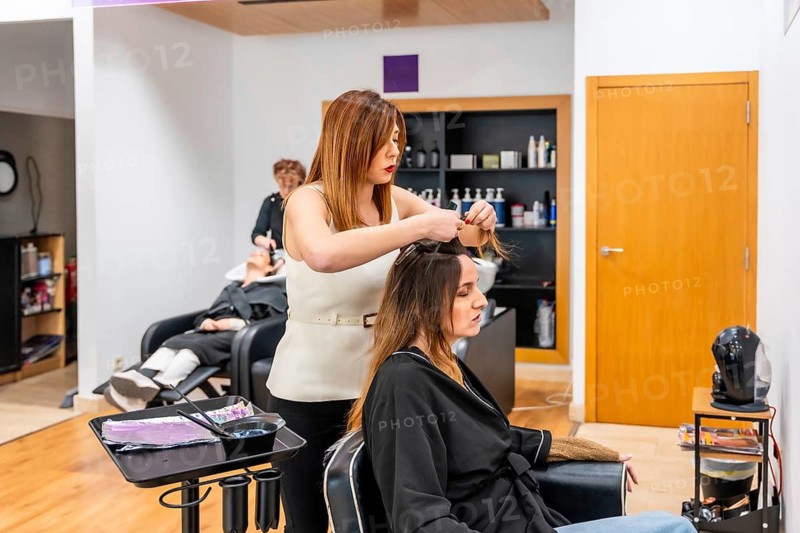 Hairdresser working on a female client's hair, carefully sectioning it for a treatment in a professional beauty salon setting with products in the background