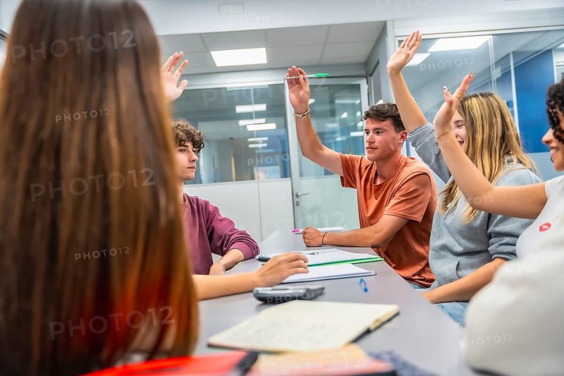 Young students in a modern classroom eagerly raise hands during an interactive lecture, collaborating, engaging in discussion and learning together with focus and enthusiasm
