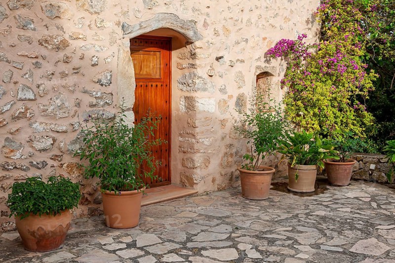 Rustic stone façade with wooden door and decorative flower pots in the courtyard, Majorca, Balearic Islands, Spain