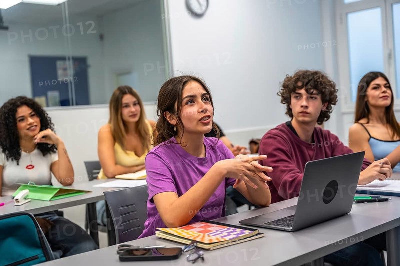 Young female student articulating her thoughts and opinions during a classroom lecture, engaging with her classmates and the instructor in a college setting