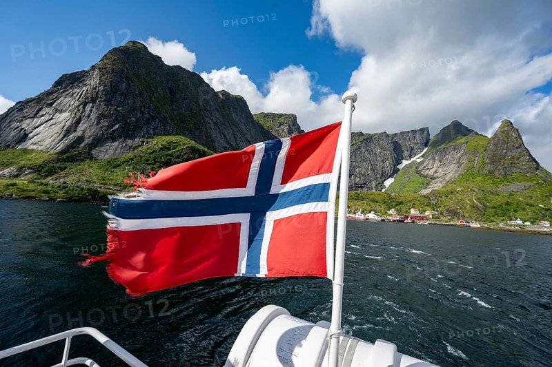 Boat trip on Reinefjord, Norwegian flag and fjord landscape with mountains, Lofoten, Norway