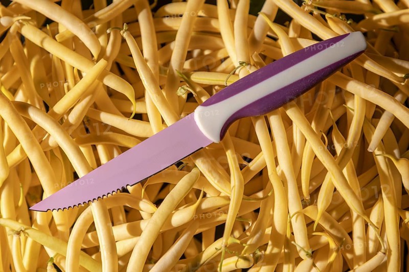 A purple knife is lying on a heap of yellow beans